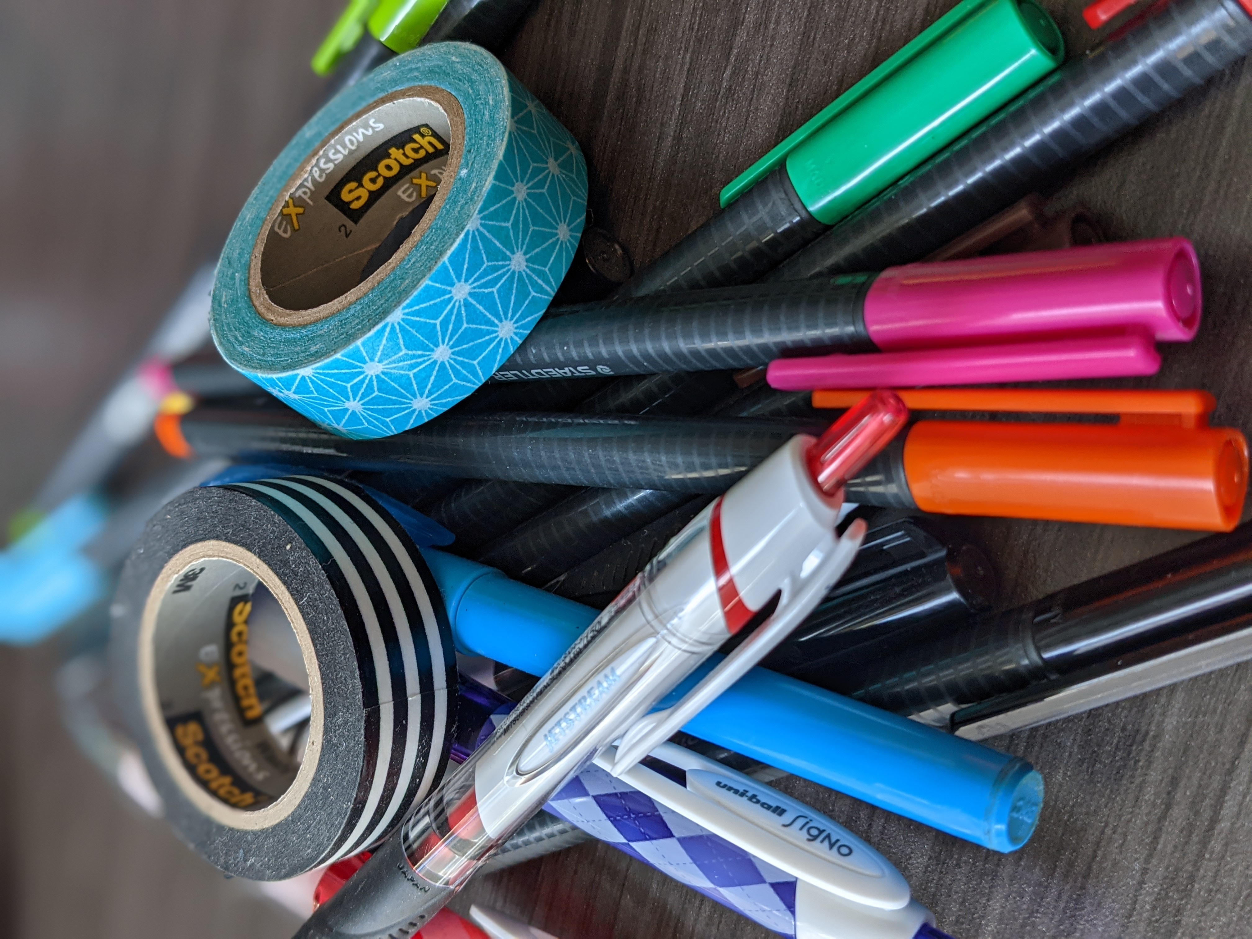 A pile of multi-colored pens and a couple of rolls of washi tape